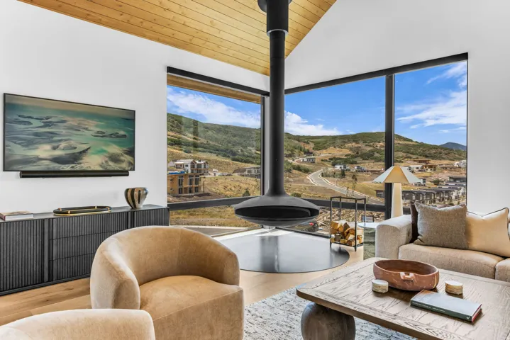 Vaulted wood-finish ceiling, expansive floor-to-ceiling windows, suspended fireplace, and wood-finish flooring