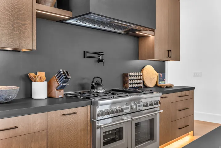 Stainless steel professional-grade range, dark countertops, wood-finish cabinetry, dark backsplash, and built-in pot filler