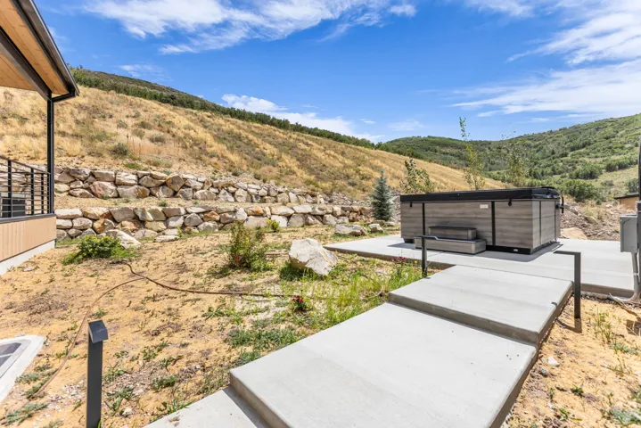 Outdoor spa with steps, surrounded by concrete pathways and a rock retaining wall