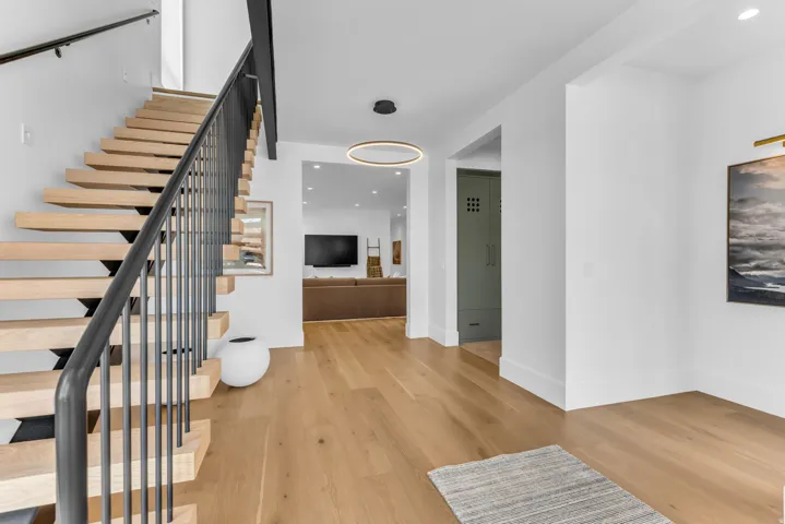 Hardwood flooring throughout, modern floating staircase with black metal railing, contemporary ceiling light fixture, recessed lighting, and built-in cabinetry