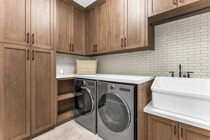 Custom cabinetry with integrated storage, white countertops, subway tile backsplash, and a large utility sink with matte black fixtures