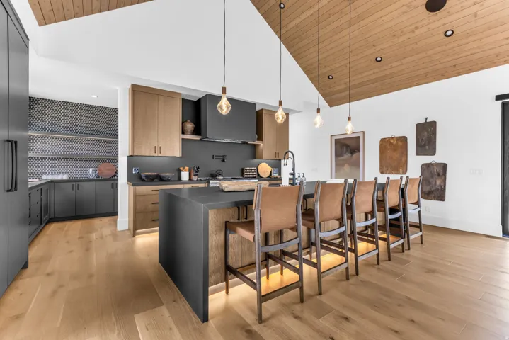 Vaulted wood-paneled ceiling, wood-finish flooring, island with integrated seating, gray cabinetry, and patterned tile backsplash