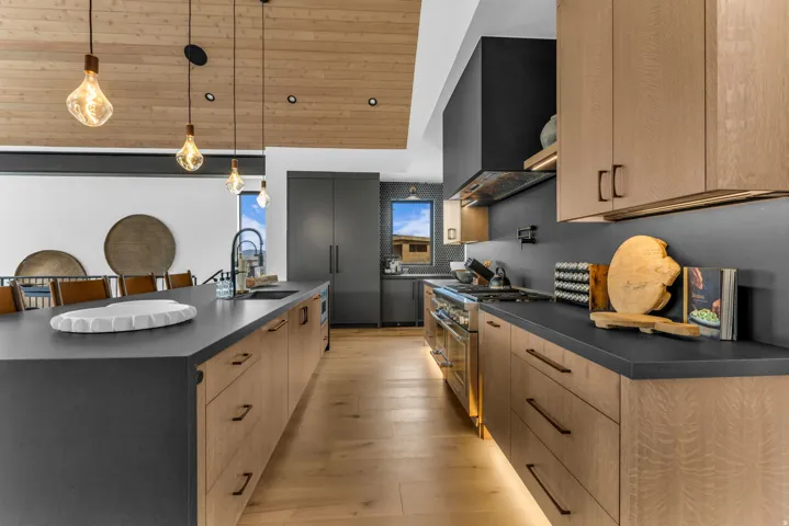 Contemporary kitchen featuring wood-finish flooring, dark countertops, wood cabinetry, a range hood, and a built-in oven