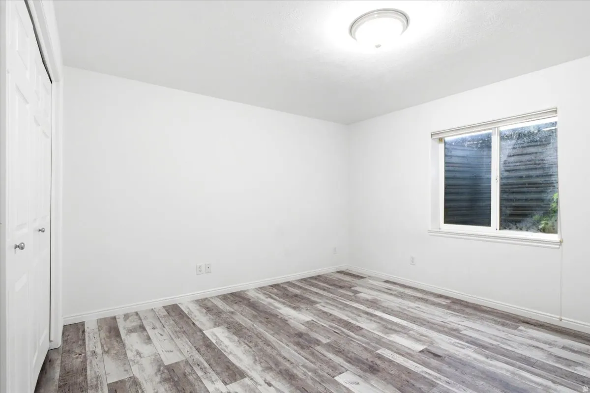 Bedroom 5. Wood-finish flooring throughout, bright white walls, and a recessed ceiling light fixture