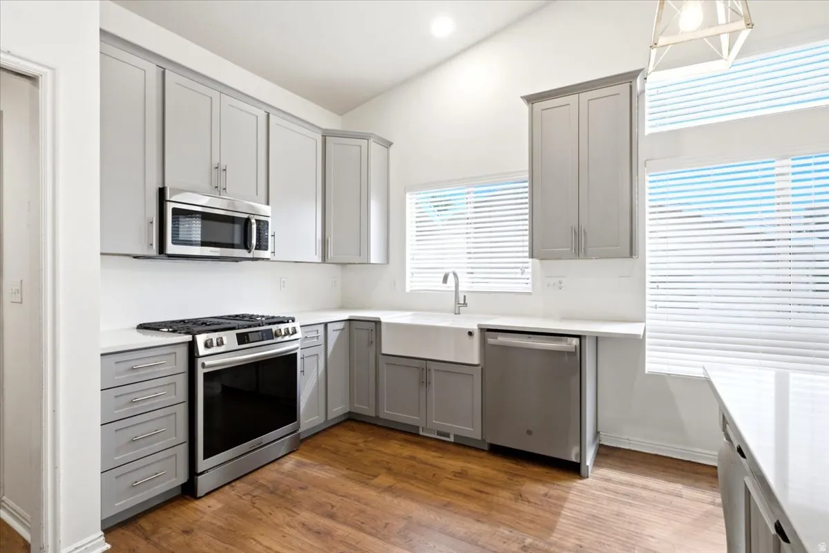 Kitchen featuring wood-finish flooring, shaker-style cabinetry, stainless steel appliances, a farmhouse sink, and granite countertops