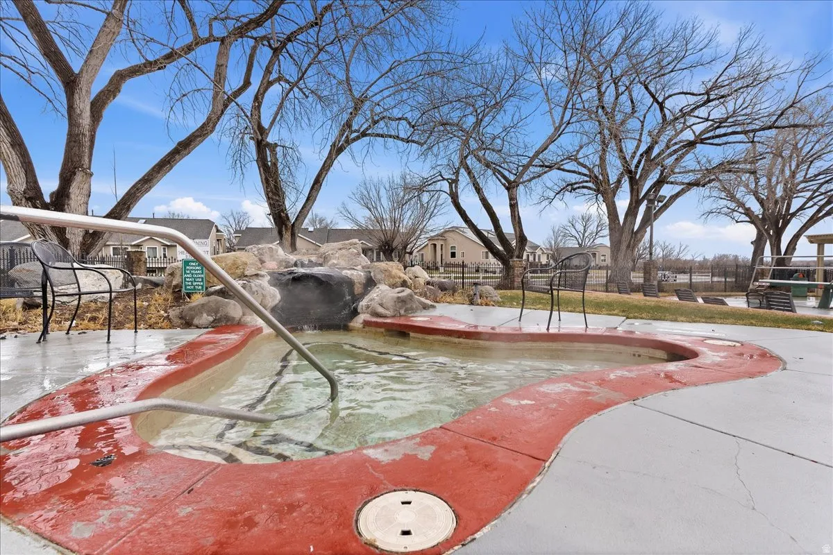 Curved spa with integrated rock water feature, surrounding concrete decking, and metal handrails