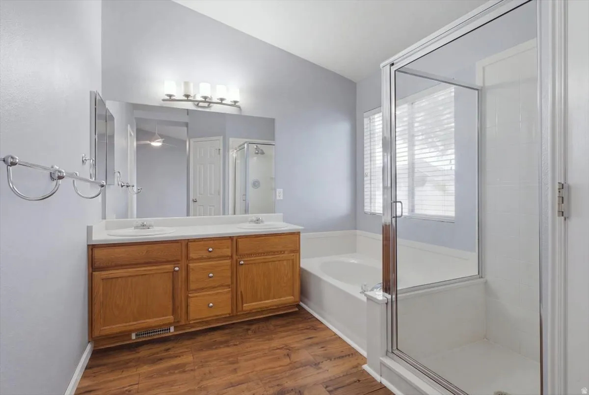 Dual basin vanity with wood-finish cabinetry, a large mirror, a separate shower enclosure, and a built-in bathtub