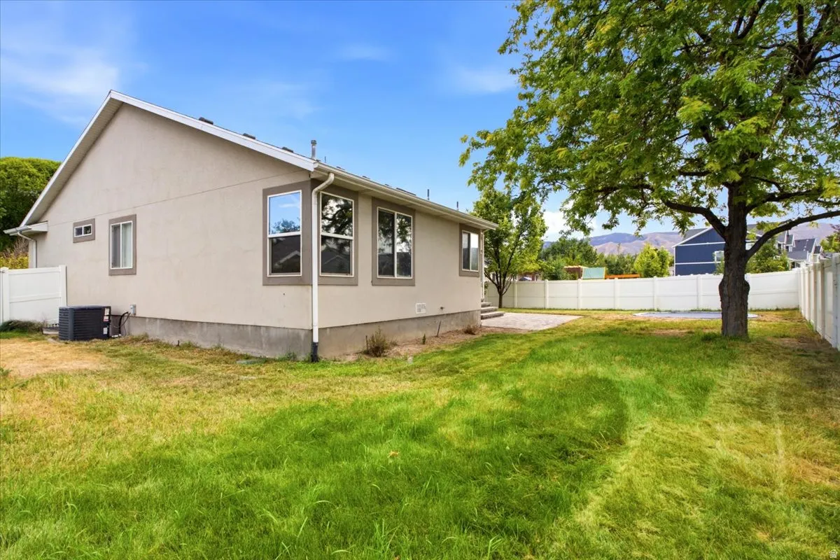 Expansive backyard featuring a mature tree, white vinyl fencing, and a concrete patio area