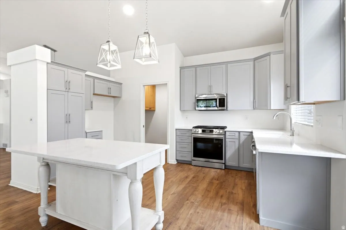 Kitchen featuring wood-finish flooring, updated cabinetry, granite countertops, stainless steel appliances, and a central island with a granite countertop