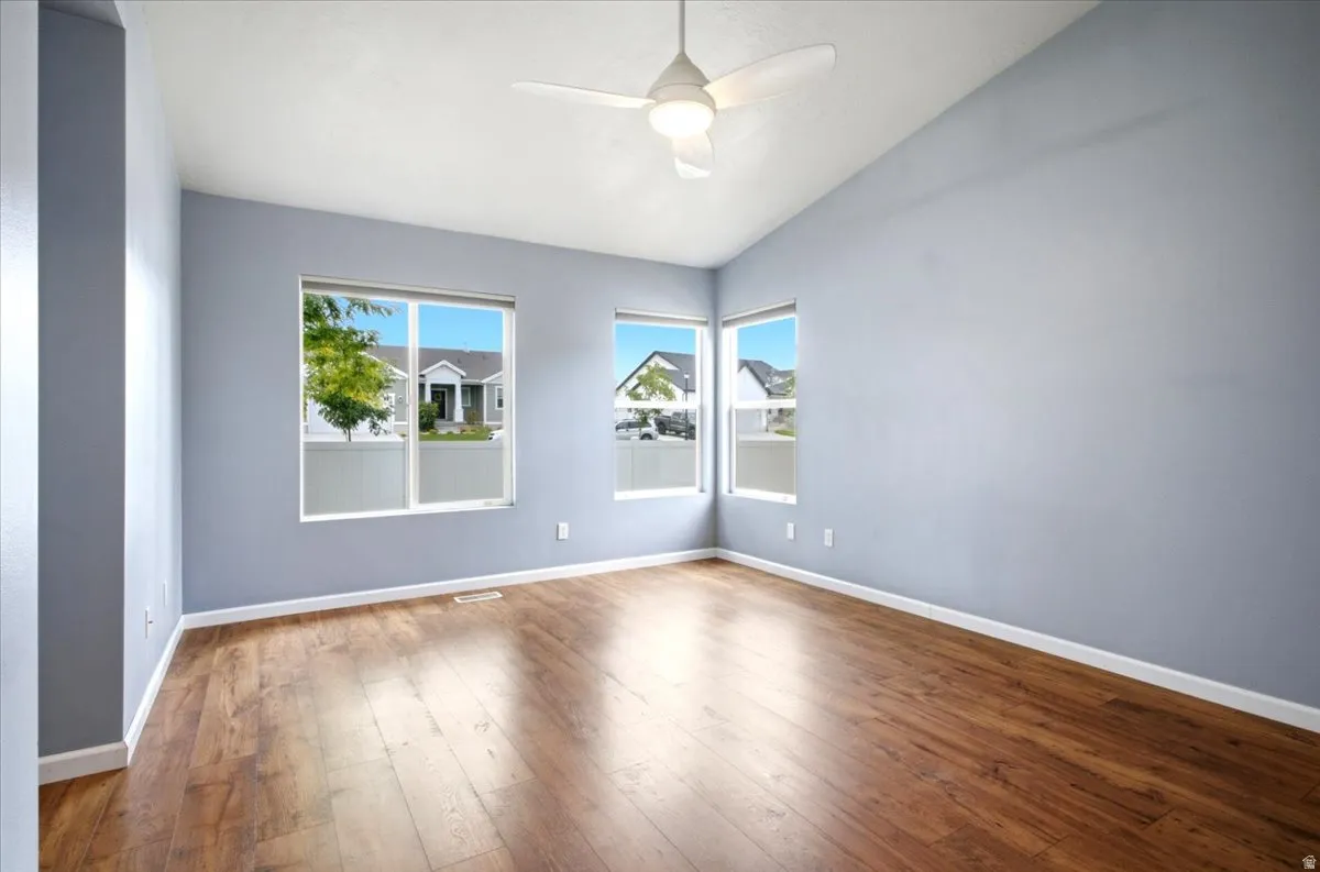 Vaulted ceilings with a ceiling fan, multiple windows, and rich wood-finish flooring