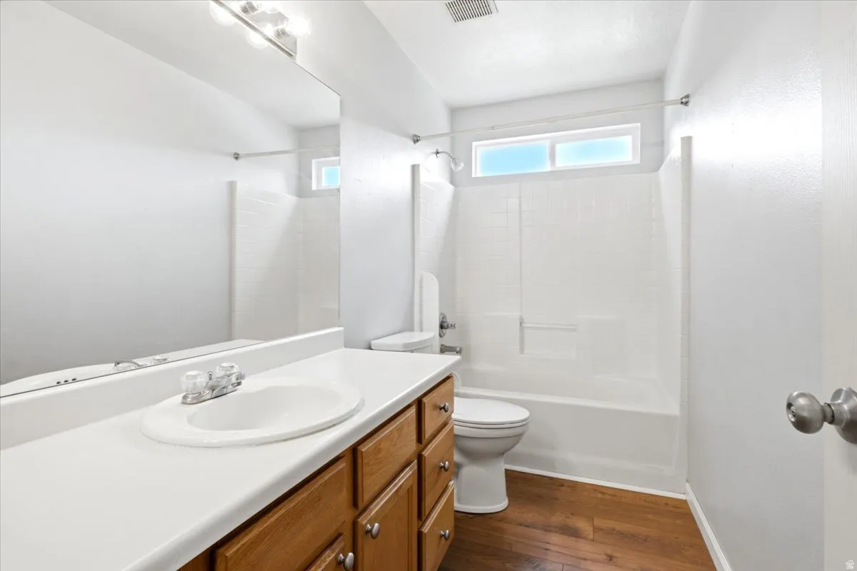 Bathroom featuring a vanity with a white countertop, wood-finish cabinetry, a built-in tub/shower combination, and wood-finish flooring