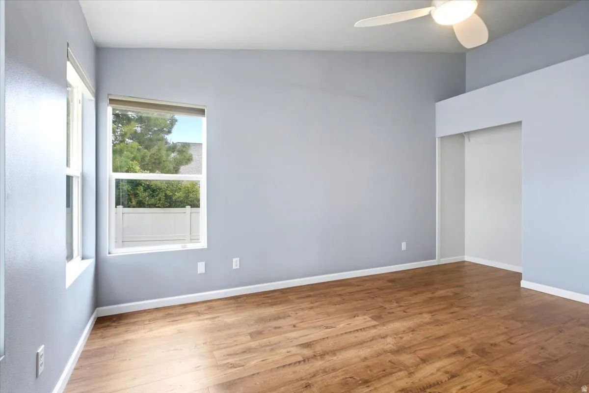 Wood-finish flooring with light-toned walls, a vaulted ceiling, and a ceiling fan