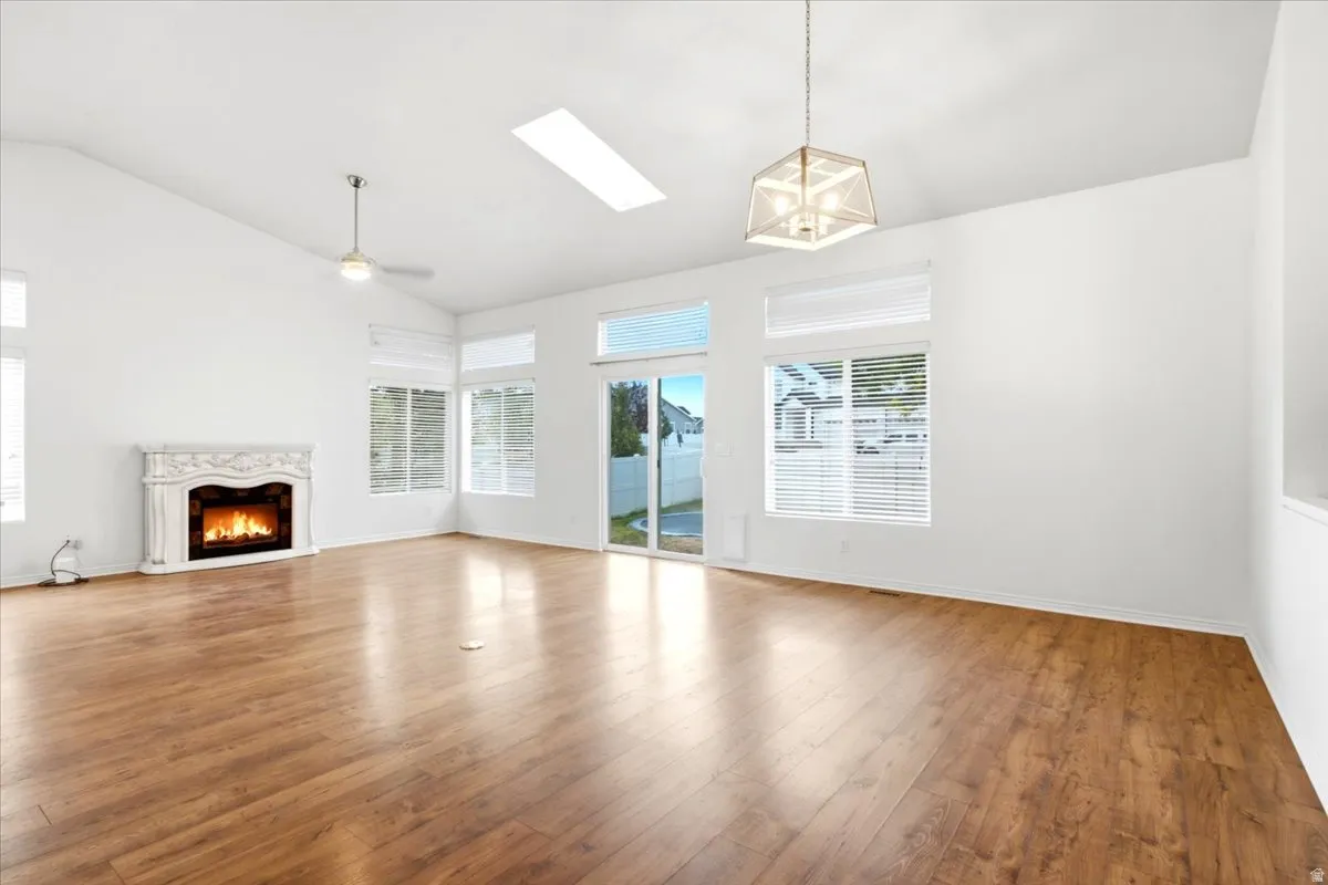 Vaulted ceilings, wood-finish flooring, a fireplace with a decorative mantel, multiple windows with blinds, and a skylight