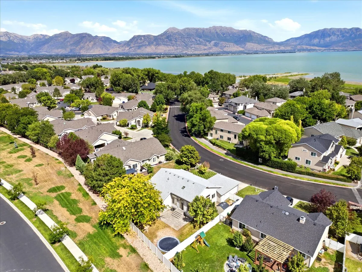 Residential neighborhood with a curved street, mature trees, and open space behind, and mountain backdrop with view of Utah Lake