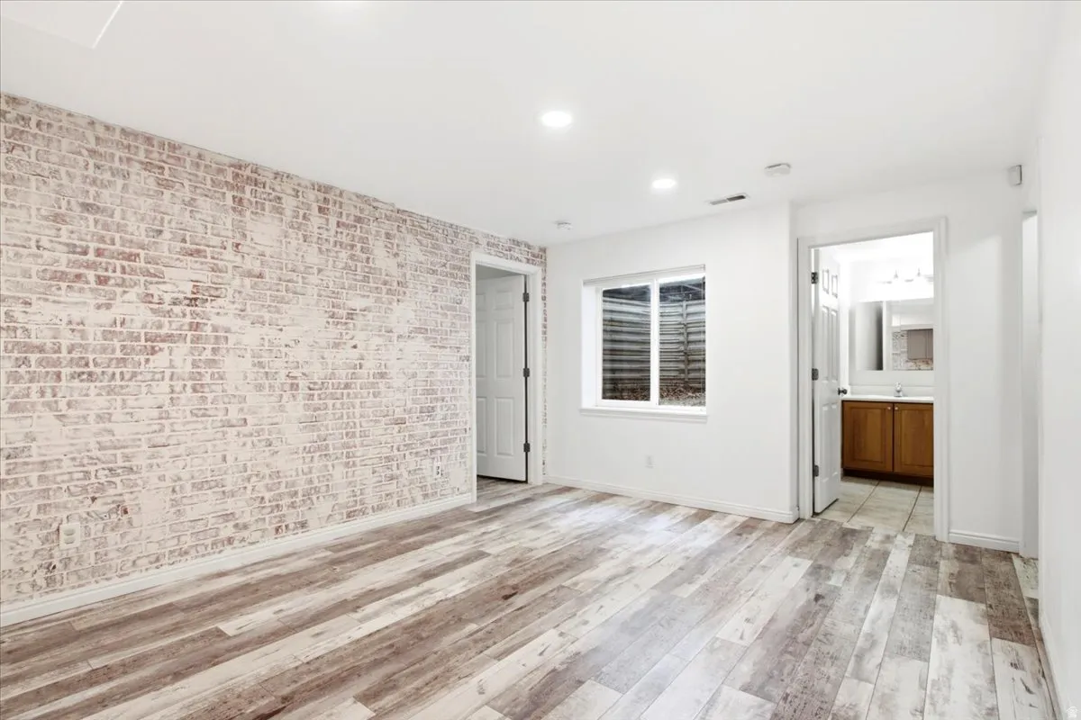 Exposed brick-finish accent wall, wood-finish flooring, recessed lighting, and a window providing natural light