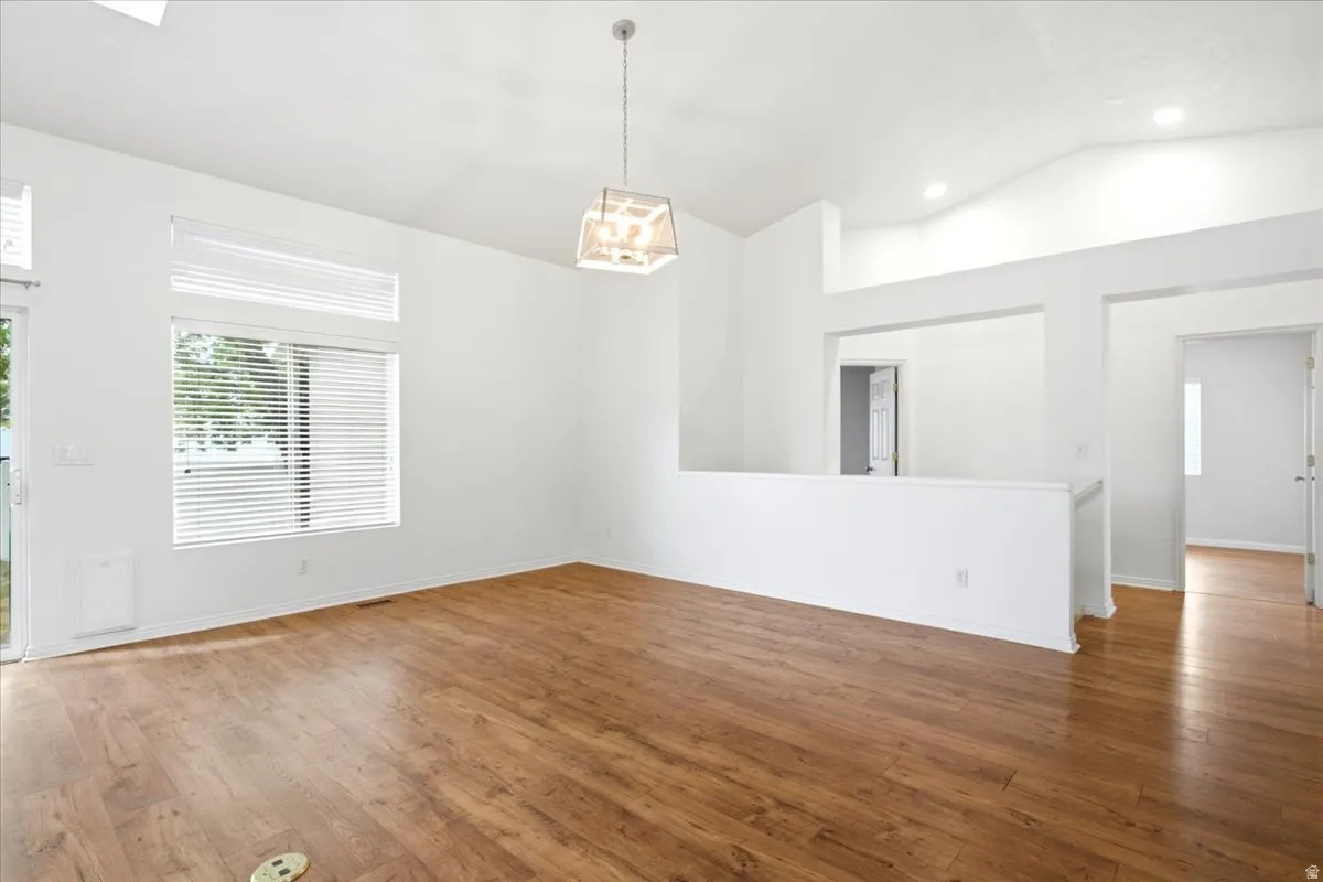 Wood-finish flooring, vaulted ceiling, pendant light fixture, recessed lighting, and large windows with blinds