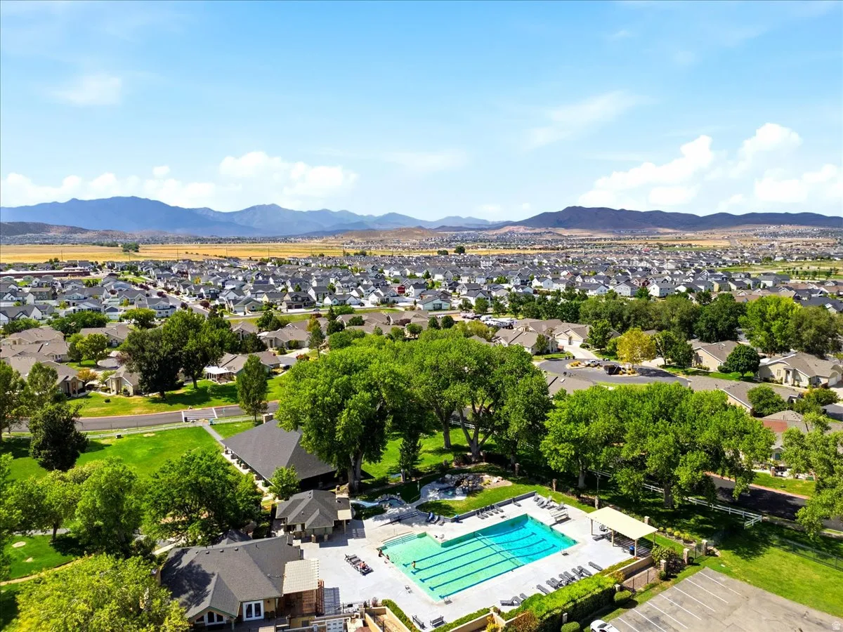 Expansive neighborhood featuring a community pool, surrounding green spaces, residential rooftops, and distant mountains
