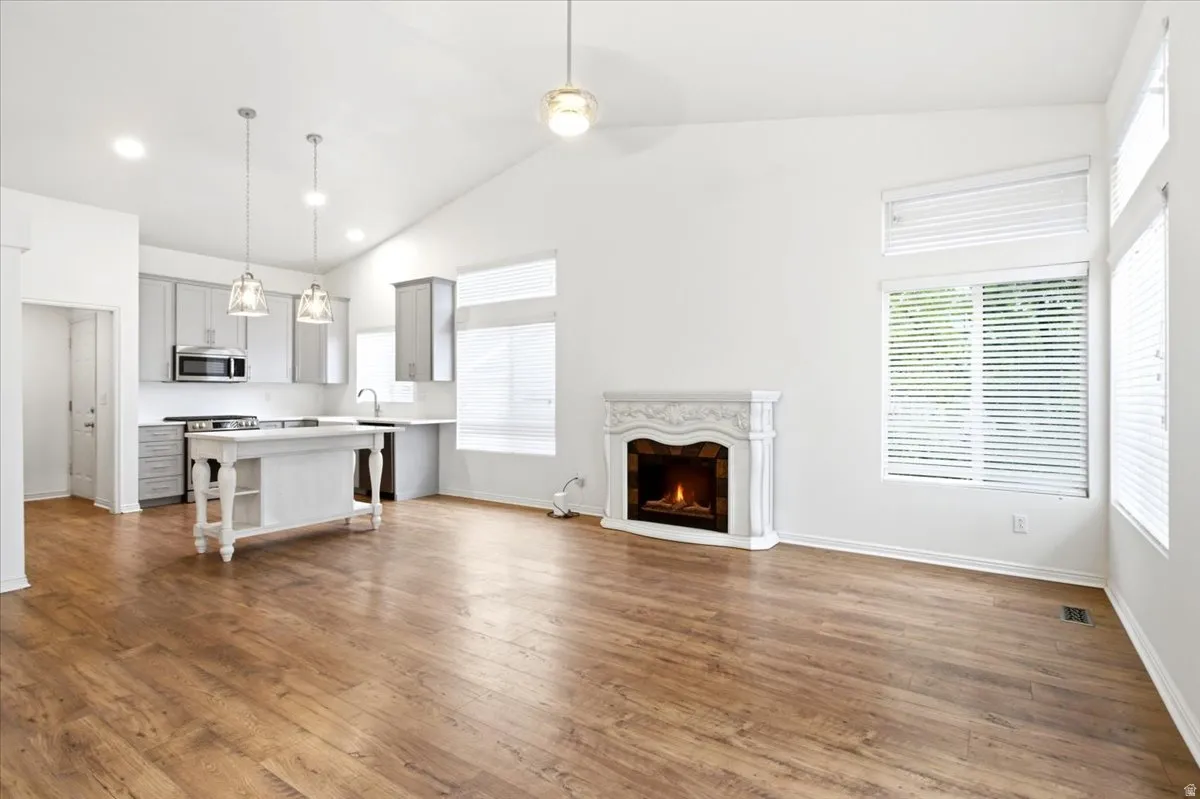 Vaulted ceiling with recessed lighting, wood-finish flooring, fireplace with decorative mantel, kitchen island with built-in shelving, and stainless steel kitchen appliances
