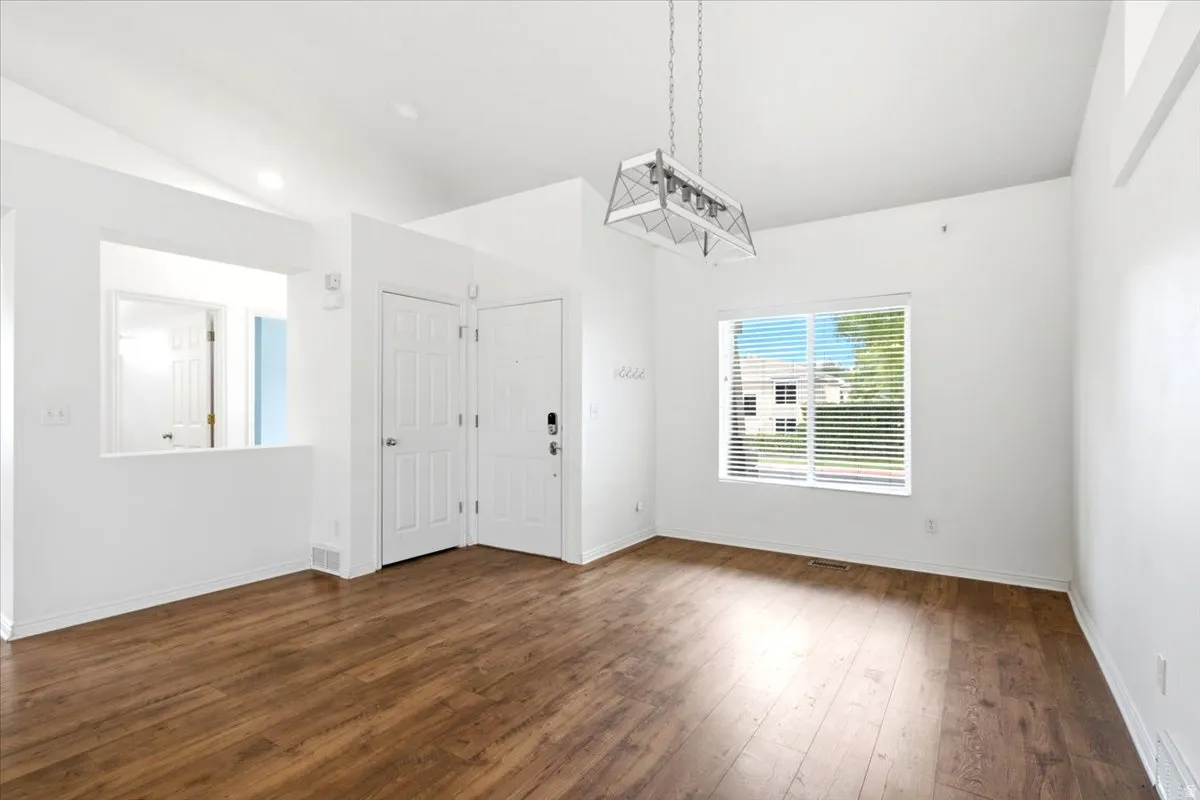 Vaulted ceiling, wood-finish flooring, white walls, rectangular window with blinds, and a decorative overhead light fixture