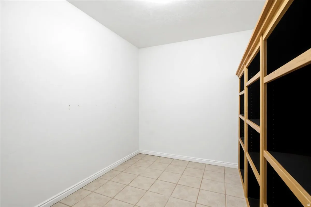 Large Storage Room Off Flex Room. Built-in wood-finish shelving with multiple compartments, neutral-toned tiled flooring, and a white ceiling