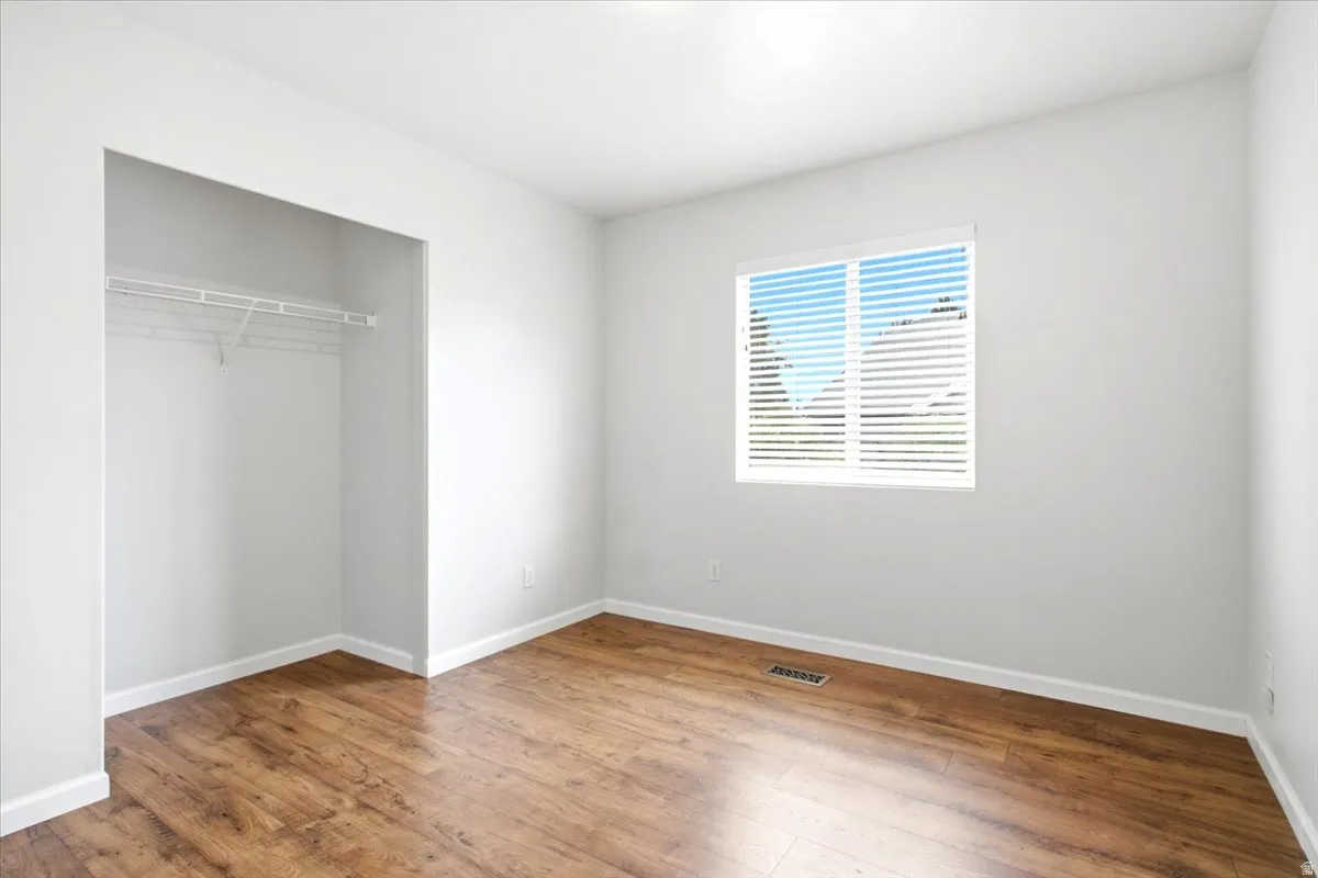 Wood-finish flooring, white walls, built-in closet shelving, and a window with horizontal blinds