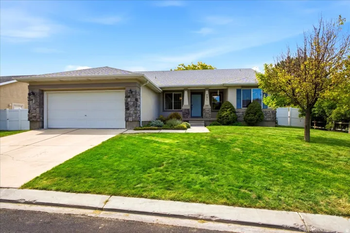 Single-story home featuring a stone facade, attached two-car garage, established landscaping, and a covered entry