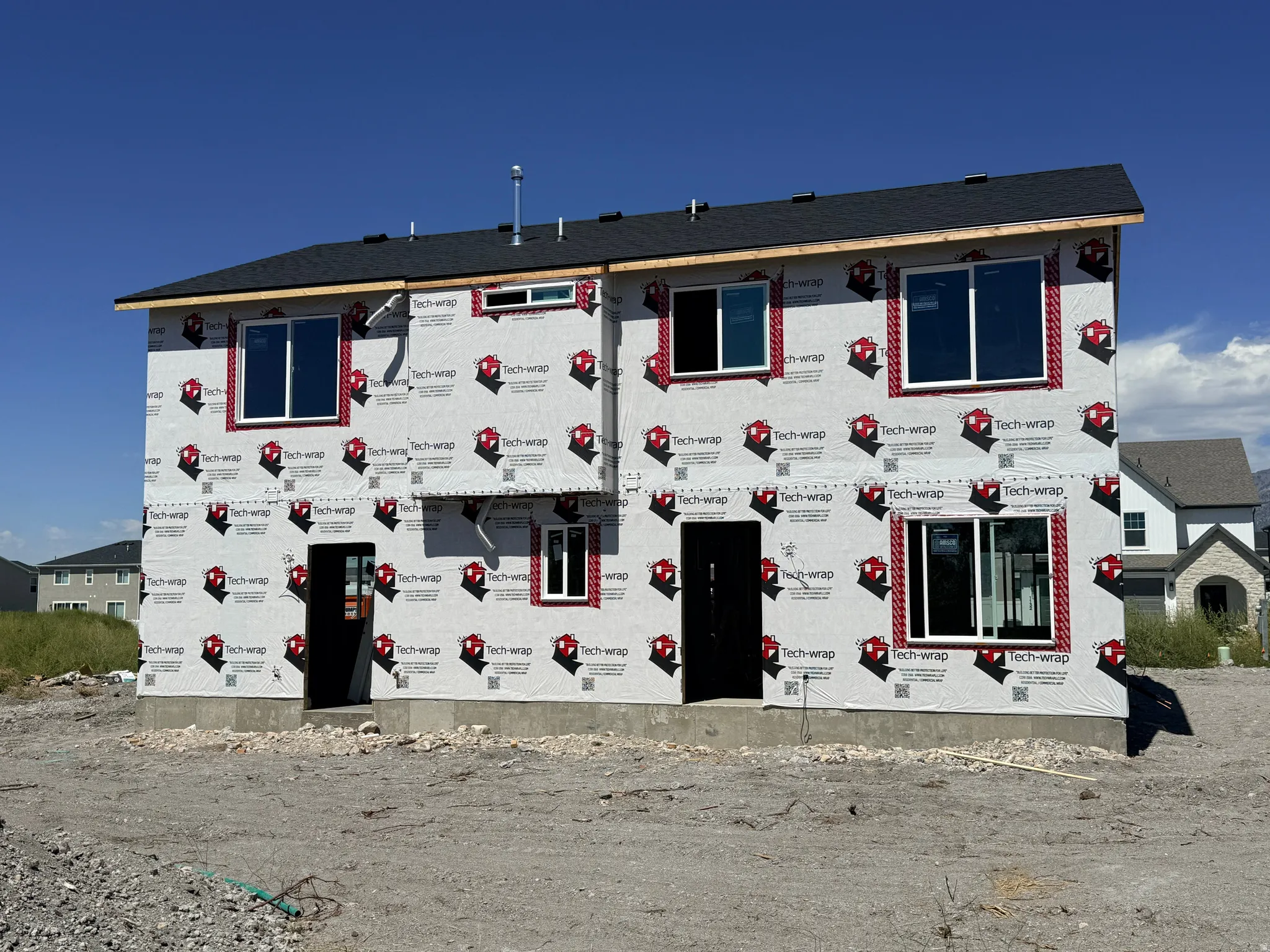 Two-story residence featuring a dark shingle roof, multiple windows with white frames, and a concrete foundation