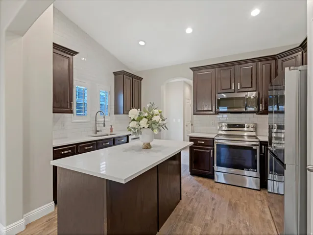Kitchen featuring dark wood cabinetry, white countertops, stainless steel appliances, a white subway tile backsplash, and wood-finish flooring