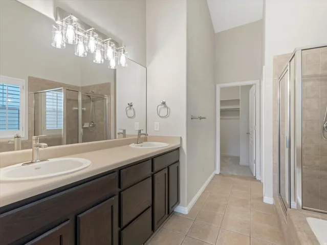 Primary suite, dual vanity with undermount sinks, contemporary light fixture, full-width mirror, tile flooring, and walk-in shower with glass enclosure