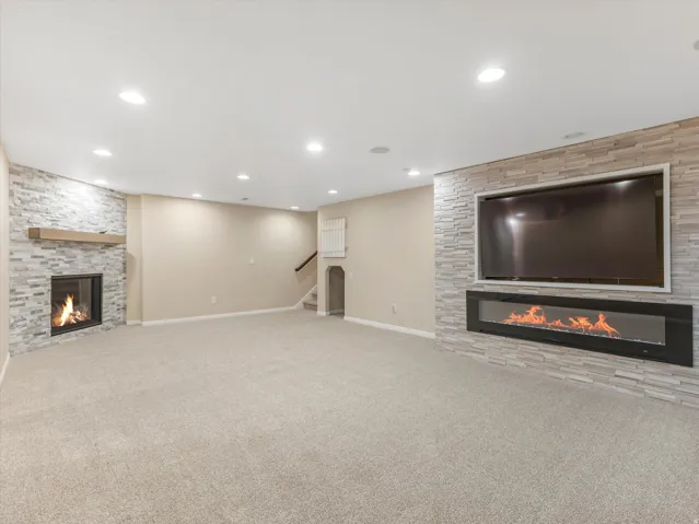 Recessed lighting, light beige carpeting, stone veneer accent wall, built-in fireplace, and staircase