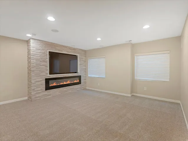 Wall-mounted electric fireplace with a stone surround, integrated television niche, recessed lighting, and carpet flooring