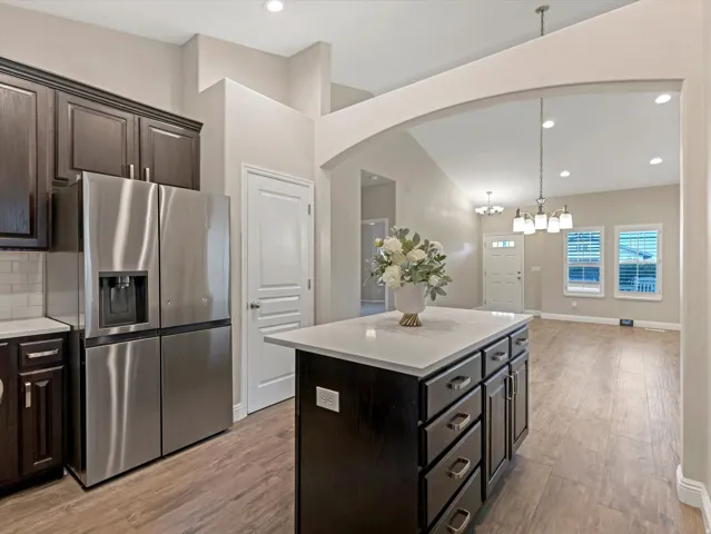 Kitchen featuring dark wood cabinetry, a stainless steel refrigerator, white tile backsplash, and wood-finish flooring