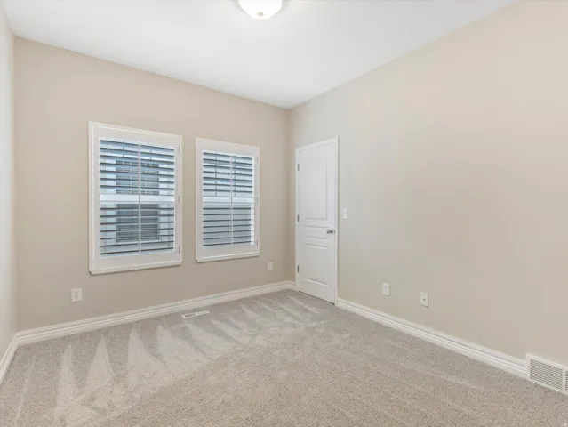 Plush carpet flooring, neutral wall tones, two windows with plantation shutters, white trim, and a ceiling-mounted light fixture