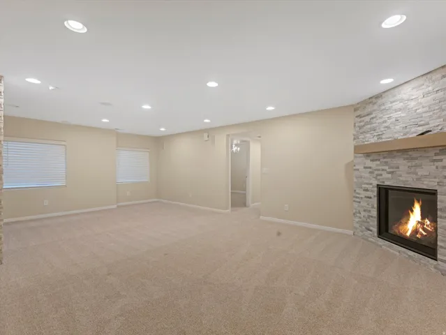 Recessed lighting, light-toned carpeting, two windows with blinds, a stone-clad fireplace, and a wood mantel