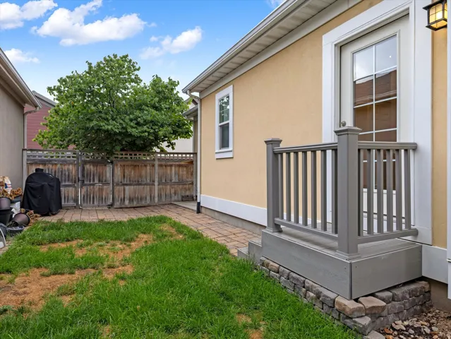 Patio with brick paver hardscaping, adjacent lawn, wooden privacy fence with gate, and stucco exterior