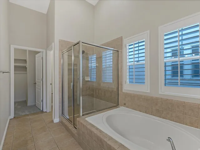 Vaulted ceiling, tiled flooring, built-in bathtub, glass-enclosed shower, and plantation shutters