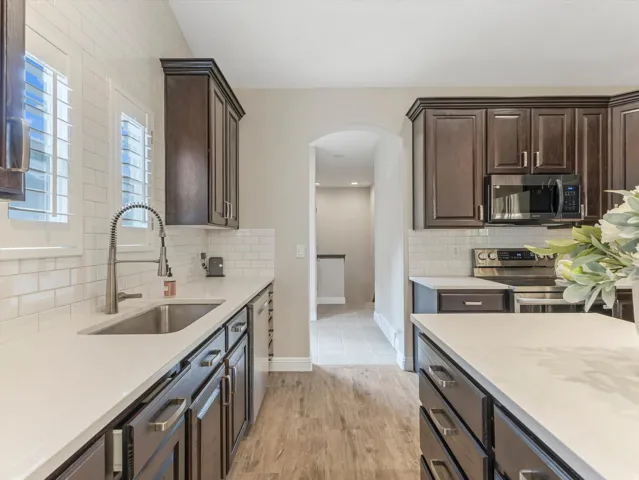 Kitchen featuring dark wood-finish cabinetry, white solid surface countertops, a subway tile backsplash, and stainless steel appliances
