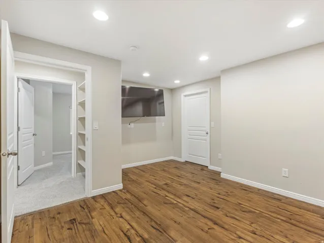 Recessed lighting illuminates the room, featuring wood-finish flooring, built-in shelving, and white trim