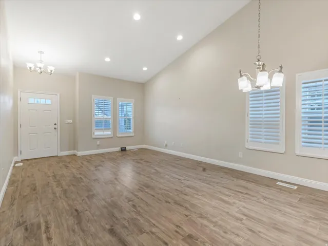 Vaulted ceiling with recessed lighting, wood-finish flooring, white door, and windows with white plantation shutters