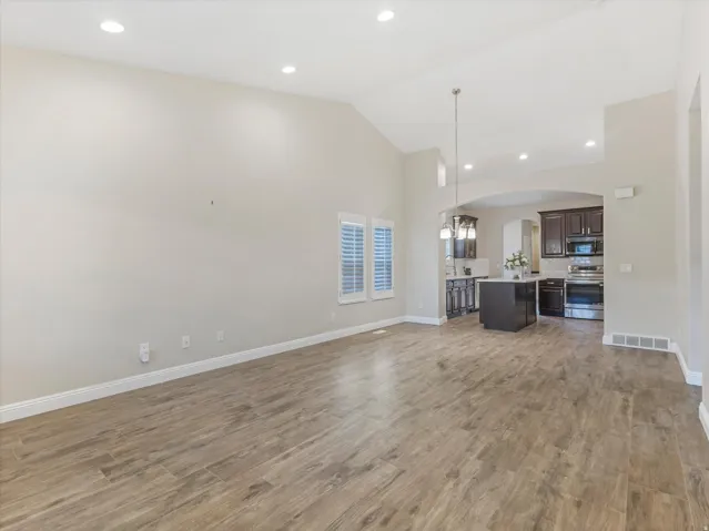Vaulted ceilings, wood-finish flooring, recessed lighting, white window shutters, and a kitchen island with pendant lighting