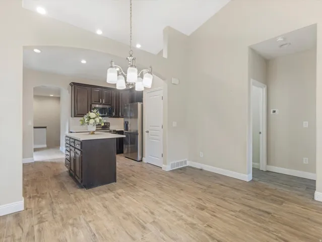 Kitchen island with dark wood cabinetry and light countertop, stainless steel appliances, wood-finish flooring, vaulted ceilings, and a decorative light fixture
