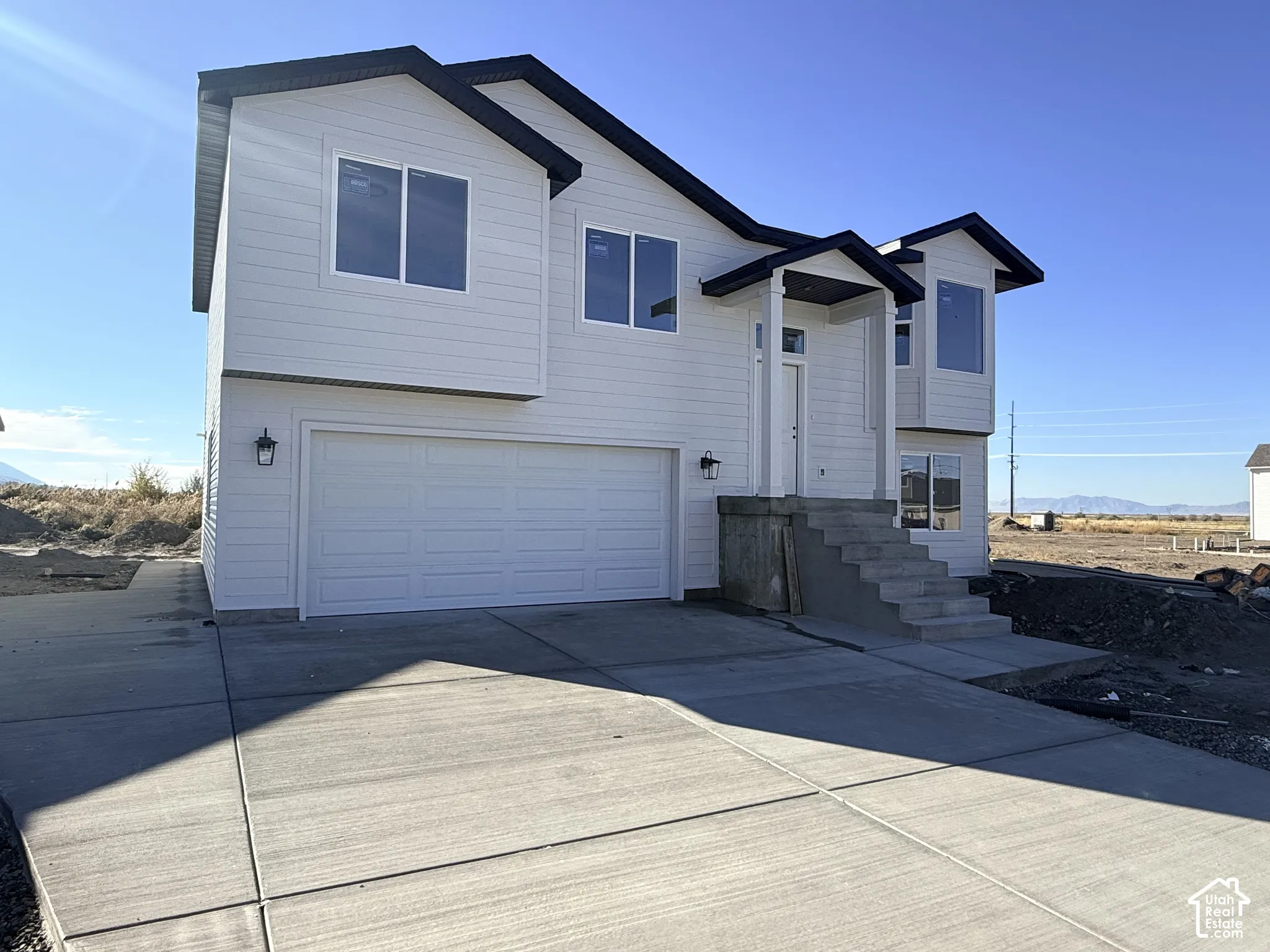 Two-story exterior featuring white horizontal siding, a multi-gabled roofline, a concrete driveway, a two-car garage, and a covered front entryway with concrete steps