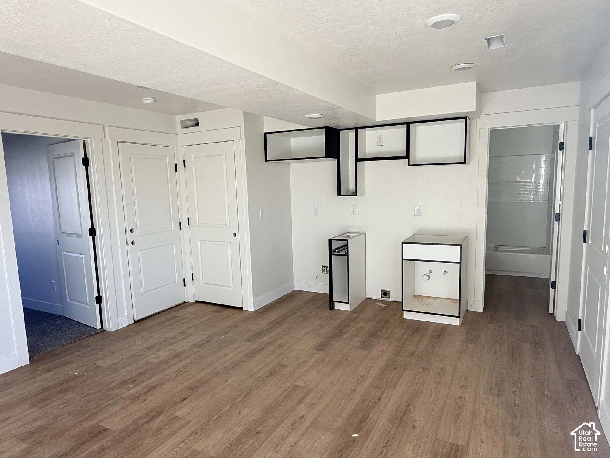 Wood-finish flooring, two-tone open cabinetry with integrated storage, and white interior doors with matte black hardware