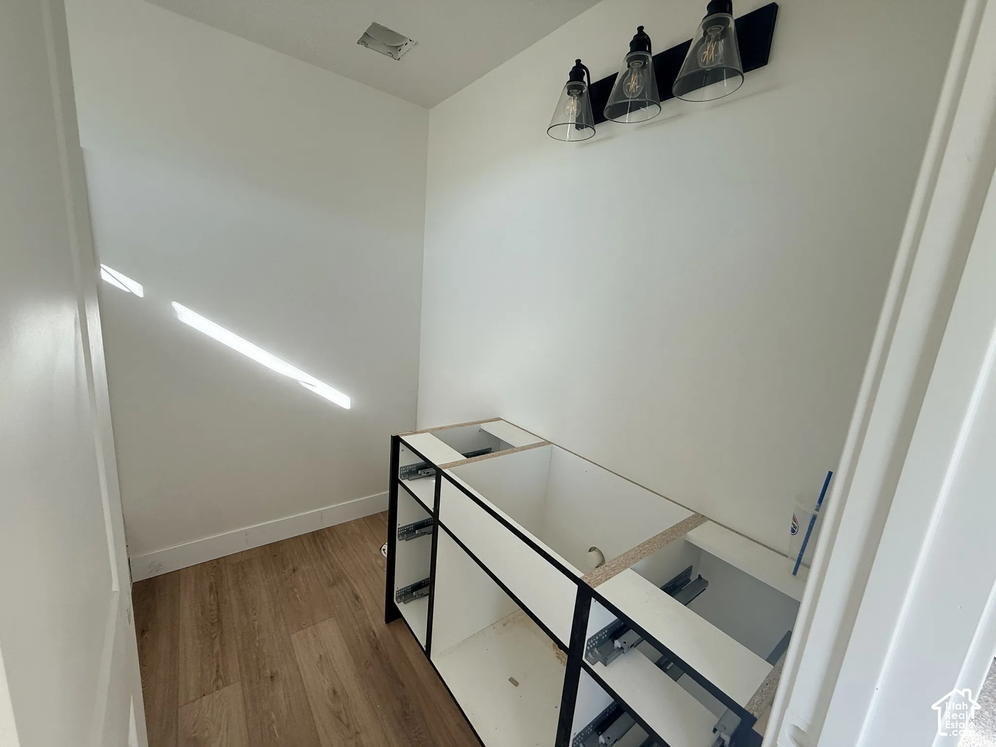 Vanity cabinet frame featuring a matte black finish, wood-finish flooring, and a three-light fixture with clear glass conical shades