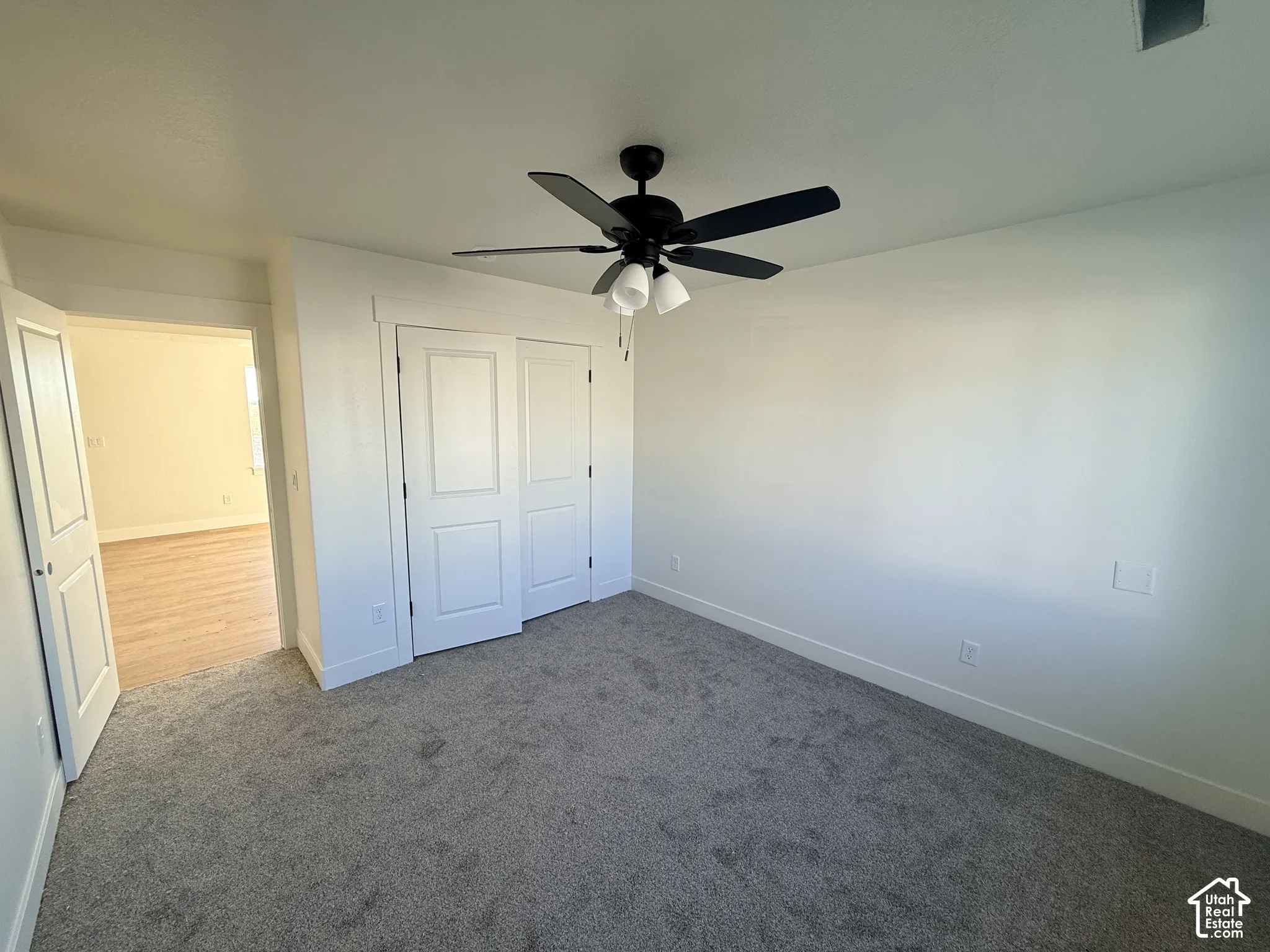Room featuring neutral carpeting, a black ceiling fan with an integrated light fixture, and two-panel interior doors