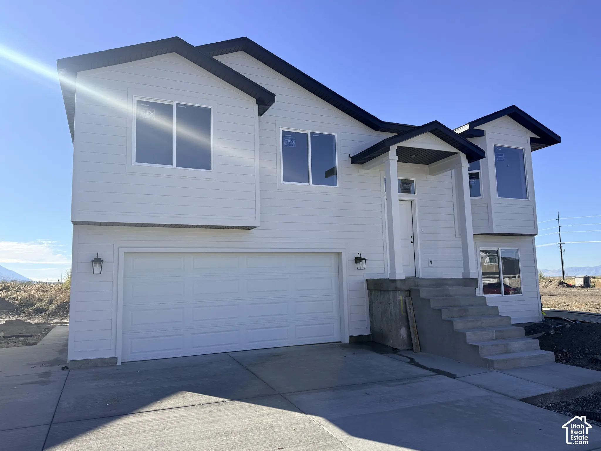 Two-story exterior featuring white horizontal siding, a gabled roofline with dark trim, a concrete driveway, and an attached two-car garage