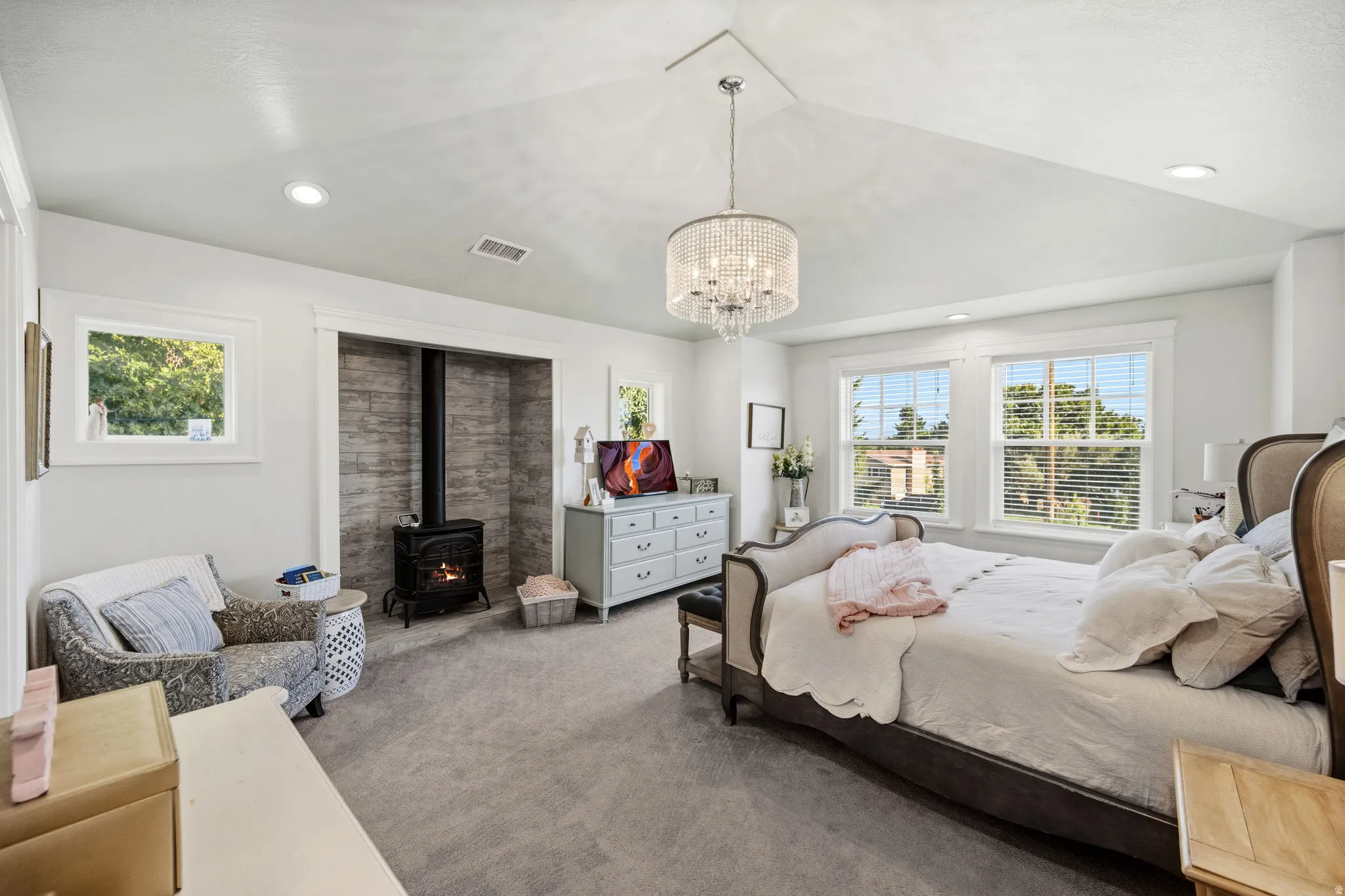 Vaulted ceilings with recessed lighting, a built-in wood stove with a stone surround, and a chandelier lighting fixture