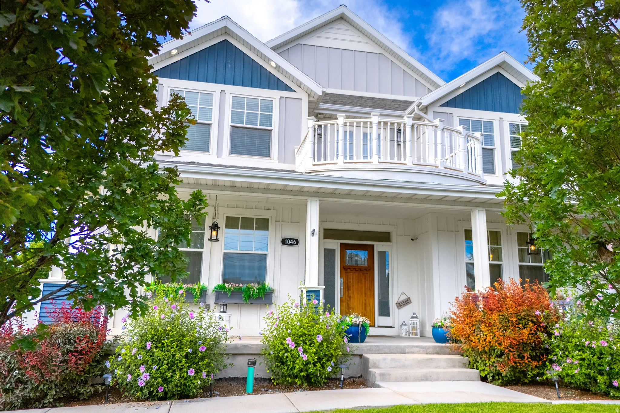 Two-story exterior featuring a balcony with white railings, a covered porch with white columns, a natural wood entry door, and dormer windows