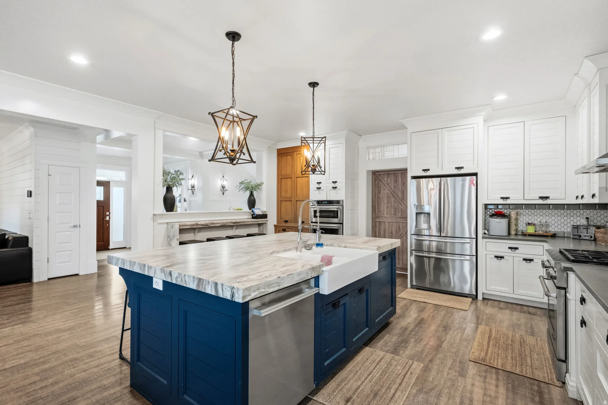 Kitchen featuring a blue island with a farmhouse sink, stainless steel appliances, white cabinetry, and wood-finish flooring