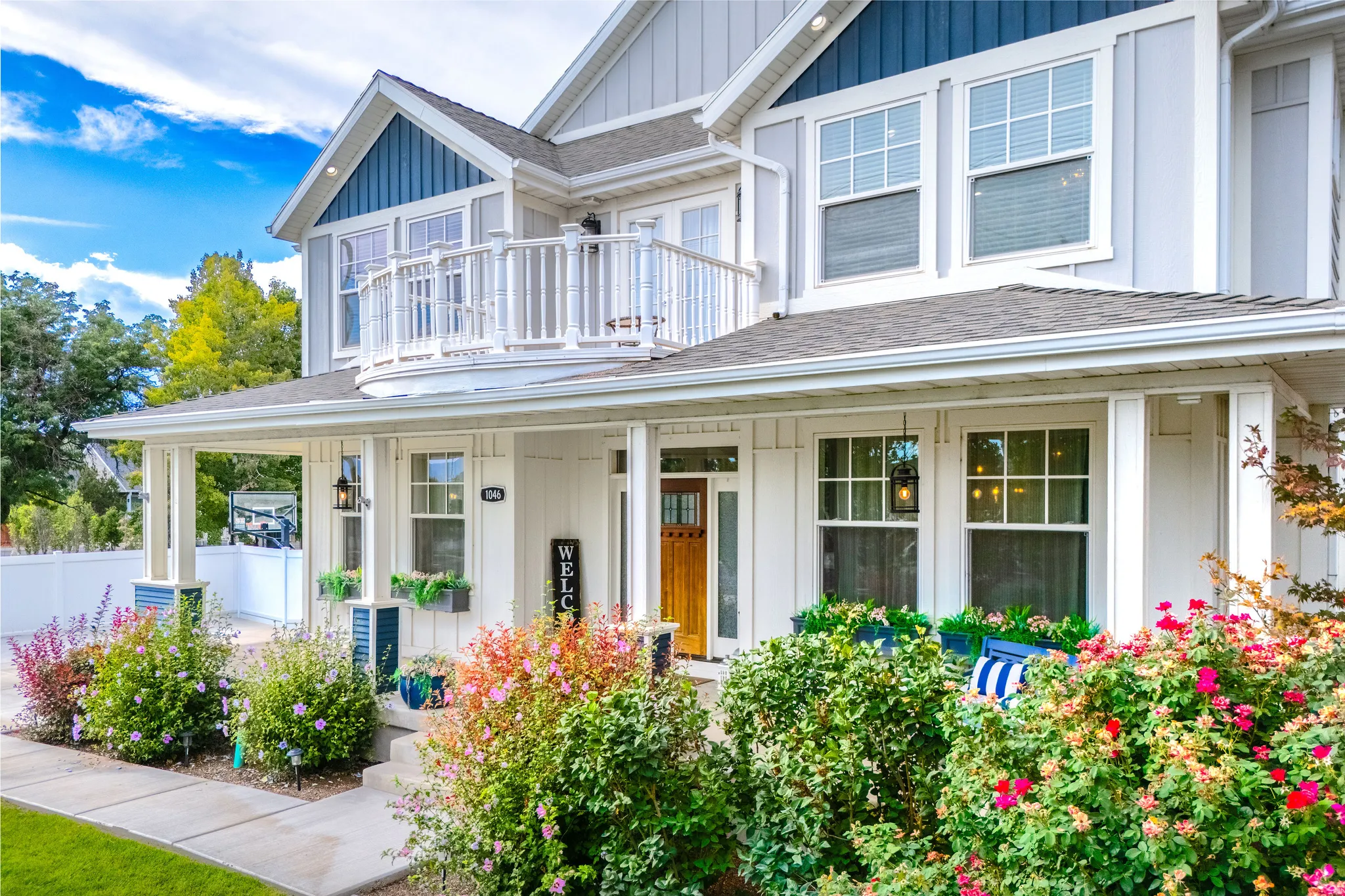 Two-story exterior with board and batten siding, second-level balcony, covered front porch, and mature landscaping